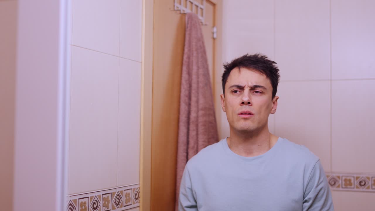 Sleepy man yawning and looking at himself in bathroom mirror