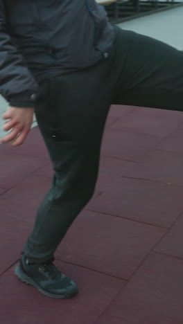 vista parcial de un atleta con capucha haciendo malabarismos con una pelota con habilidosa precisión durante el entrenamiento en una arena deportiva urbana, con fondos con bancos y paisaje urbano