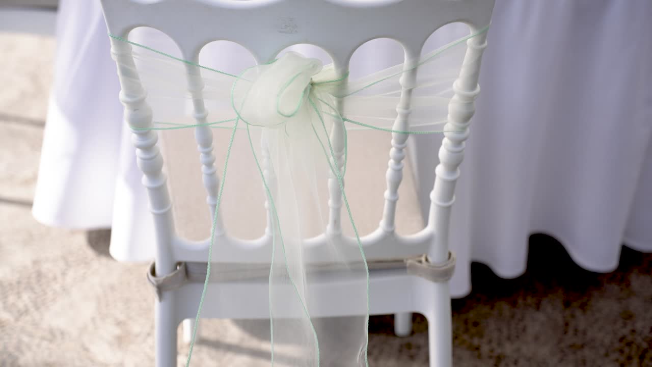In this lovely outdoor setting, a white chair is elegantly adorned with soft green ribbon, enhancing the festive atmosphere for a special occasion