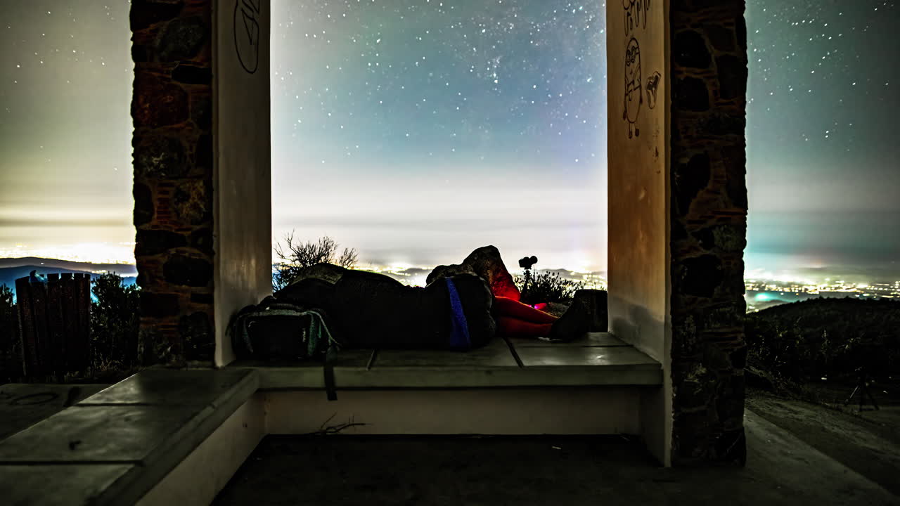 timelapse cinematográfico de una persona durmiendo mientras filma un timelapse de estrellas sobre un cielo de ciudades