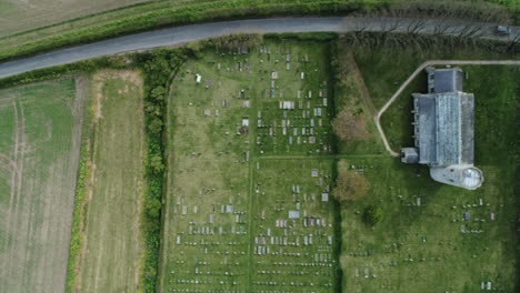 topdown aerial drone shot flying over old medieval 11th century round tower church with graveyard on cloudy day in north norfolk uk