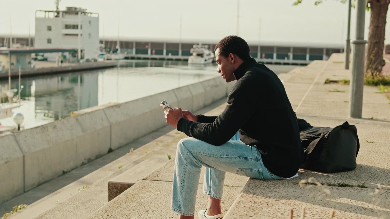 Young Man Using Smartphone While Sitting by the Harbor