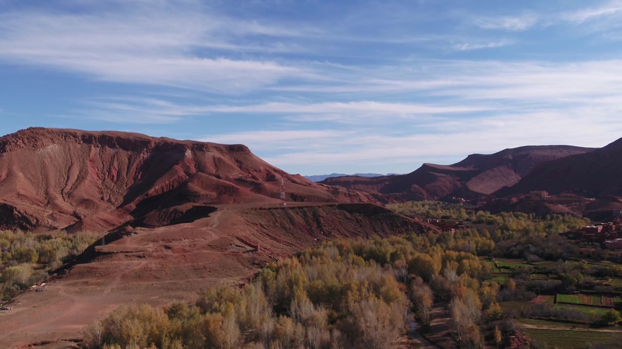 Prospettiva aerea sopraelevata che evidenzia una suggestiva formazione di mesa sedimentaria rossa e la topografia del canyon delimitata da alberi di oasi a Tinghir, Marocco