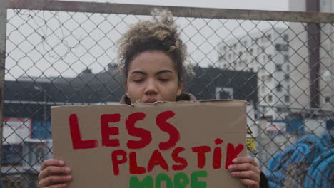 close up view of young american female activist holding a cardboard placard against the use of plastics during a climate change protest while looking at camera 1