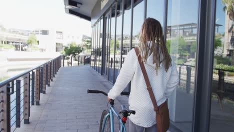 mixed race man with dreadlocks wheeling a bicycle in the street