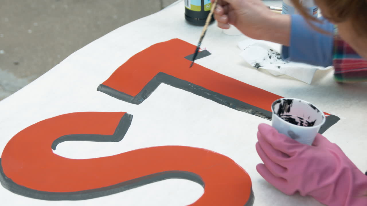 A woman finishes painting a T on a sign with black paint