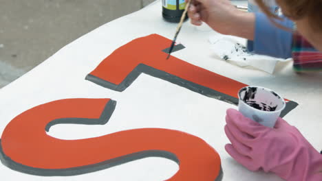 a woman finishes painting a t on a sign with black paint