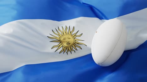 White-rugby-ball-over-waving-flag-of-argentina-with-copy-space,-in-slow-motion