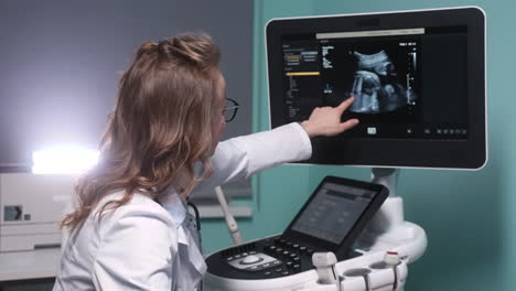 ginecólogo femenino que muestra la imagen del feto en la pantalla de la máquina de ultrasonido