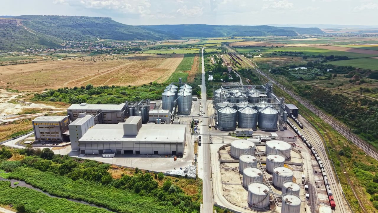 Industrial facility with storage silos and transport area near a valley under a clear sky