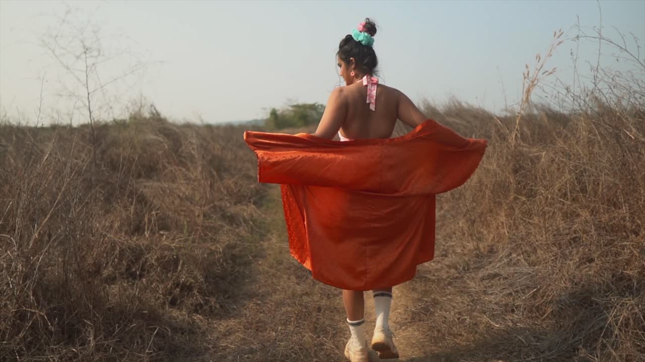 la espalda de una mujer asiática atractiva y despreocupada que abraza la libertad de la naturaleza, su camisa de gran tamaño ondea en la brisa de la mañana mientras camina por un sendero en un campo, india