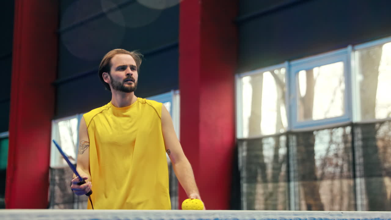 Man in yellow shirt playing pickleball on a blue, inside court