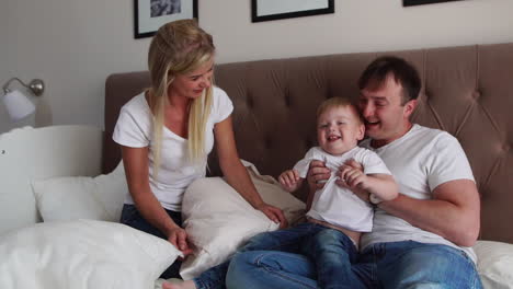 loving parents play with their son on the bed laughing and smiling in the bedroom