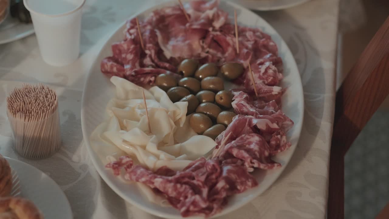 Piatto ovale con affettati di maiale, formaggio bianco e olive verdi, ideale per festeggiamenti