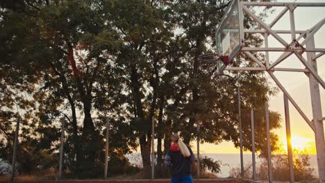 A-blonde-girl-throws-a-basketball-into-the-basket-and-scores-a-goal-on-a-red-basketball-court-while-playing-with-her-friend-at-Sunrise-in-the-morning