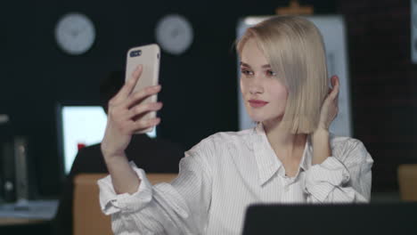 Attractive-business-woman-making-selfie-on-mobile-phone-in-dark-office