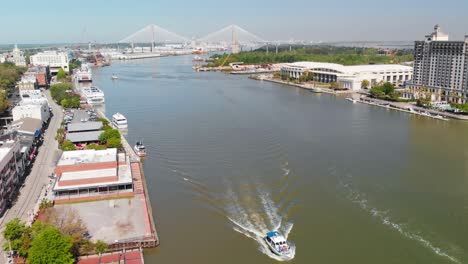 aerial view of boat moving on the savannah river with buildings lined up of both sides of the river banks