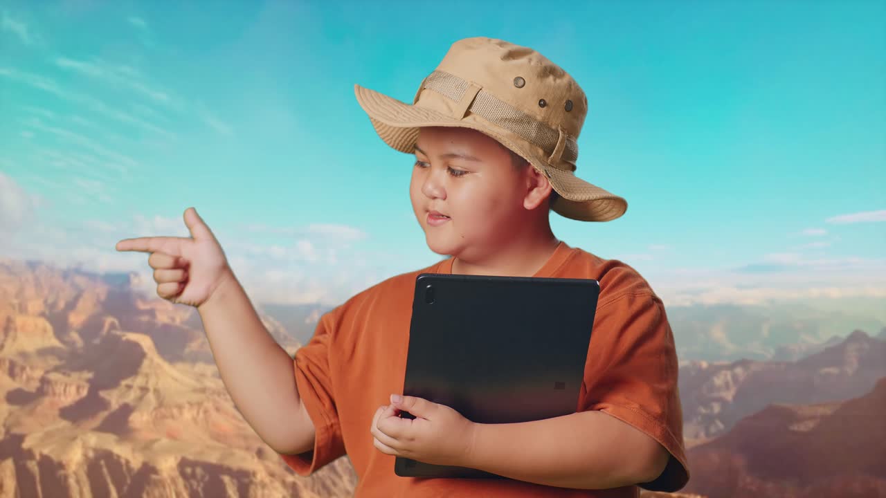 Asian Boy With A Hat And Binoculars Using A Tablet Then Smiling And Pointing To Side While Traveling At The Top Of Mountain. Boy Researcher Examines Something, Travel Adventure Concept, Close Up