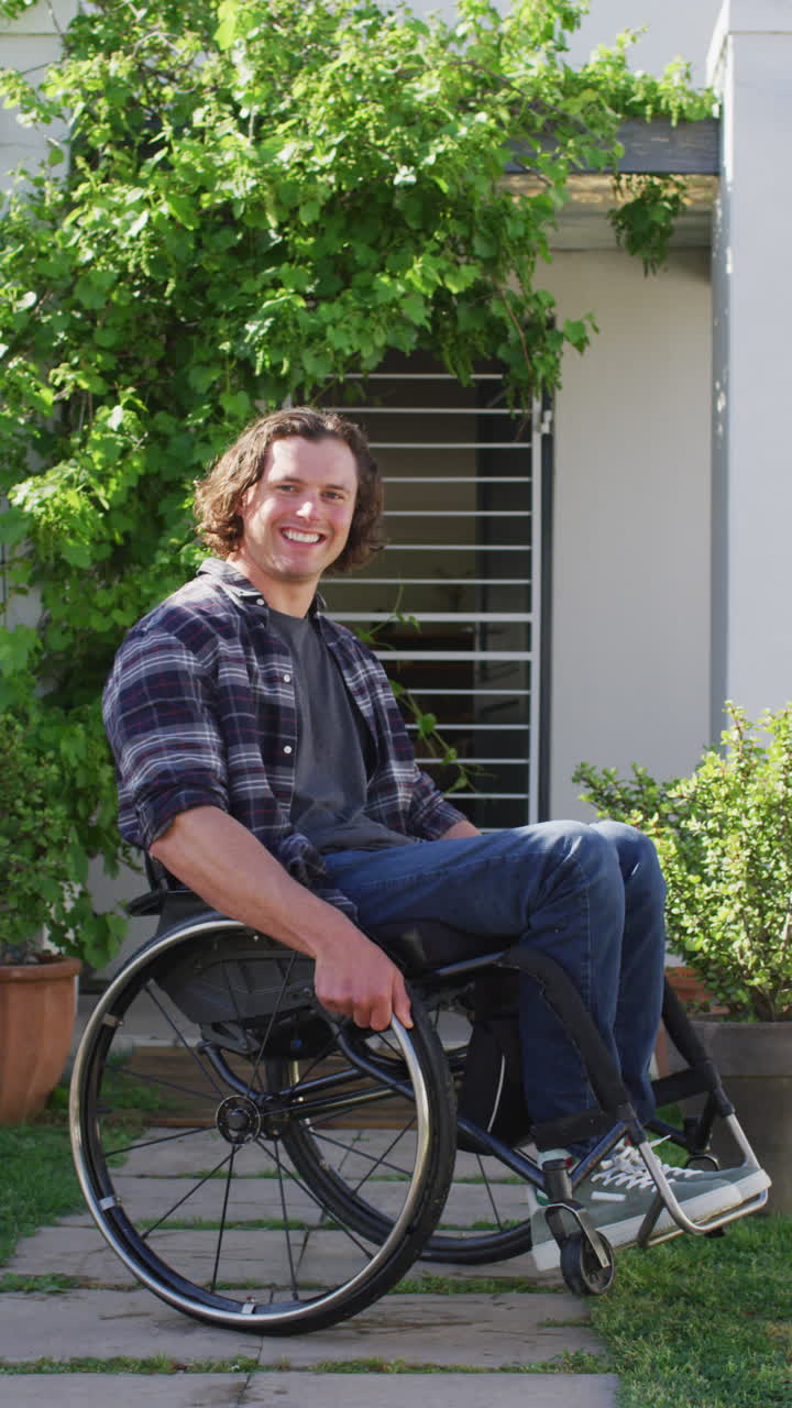 Vertical video of happy caucasian disabled man sitting in wheelchair in garden