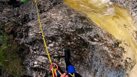 Point-of-view-shot-of-a-men-in-a-blue-and-black-wetsuit-starting-to-rappel-down-a-waterfall