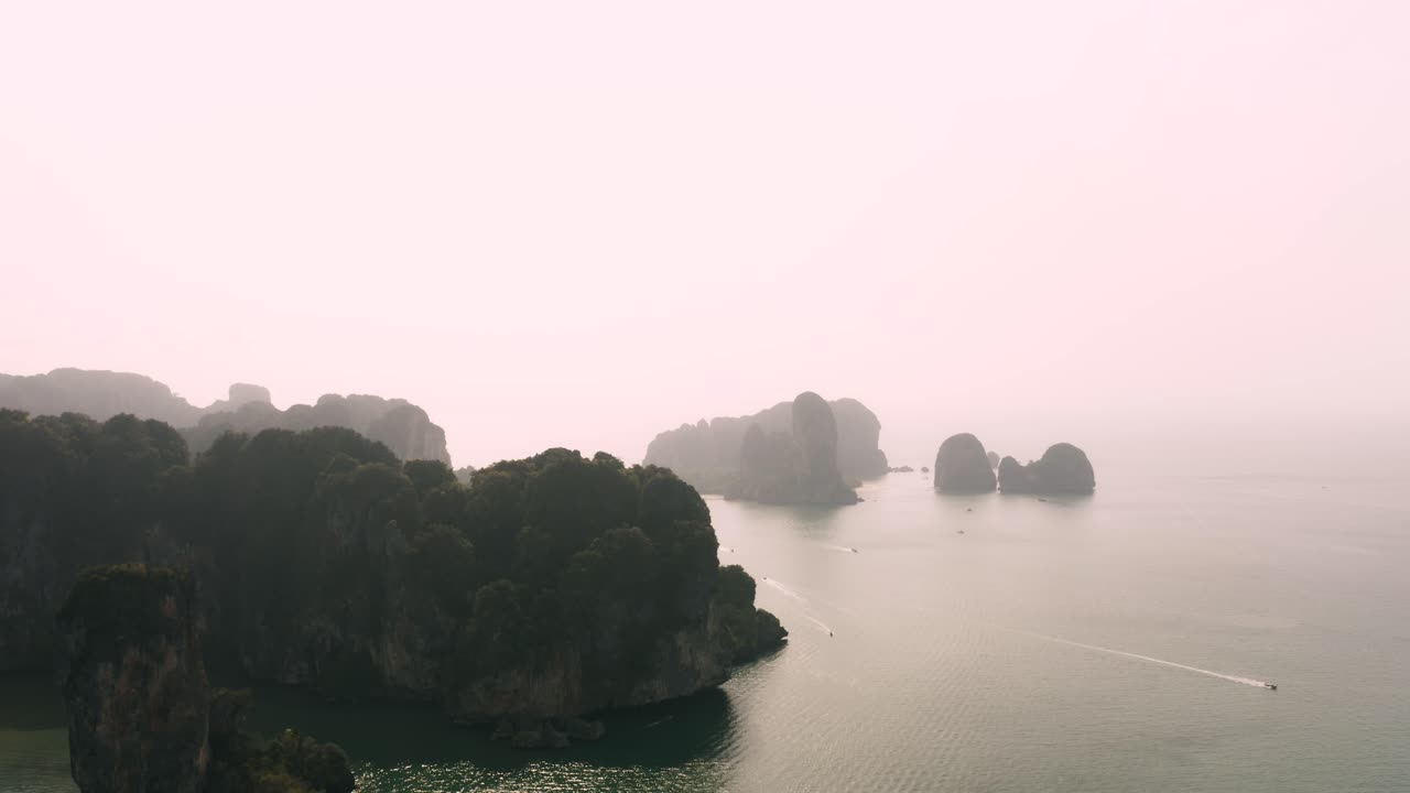 An awe-inspiring aerial view of Krabi, Thailand, where towering limestone formations emerge majestically from the mist-kissed ocean. An ideal backdrop for a documentary or a dramatic scene.