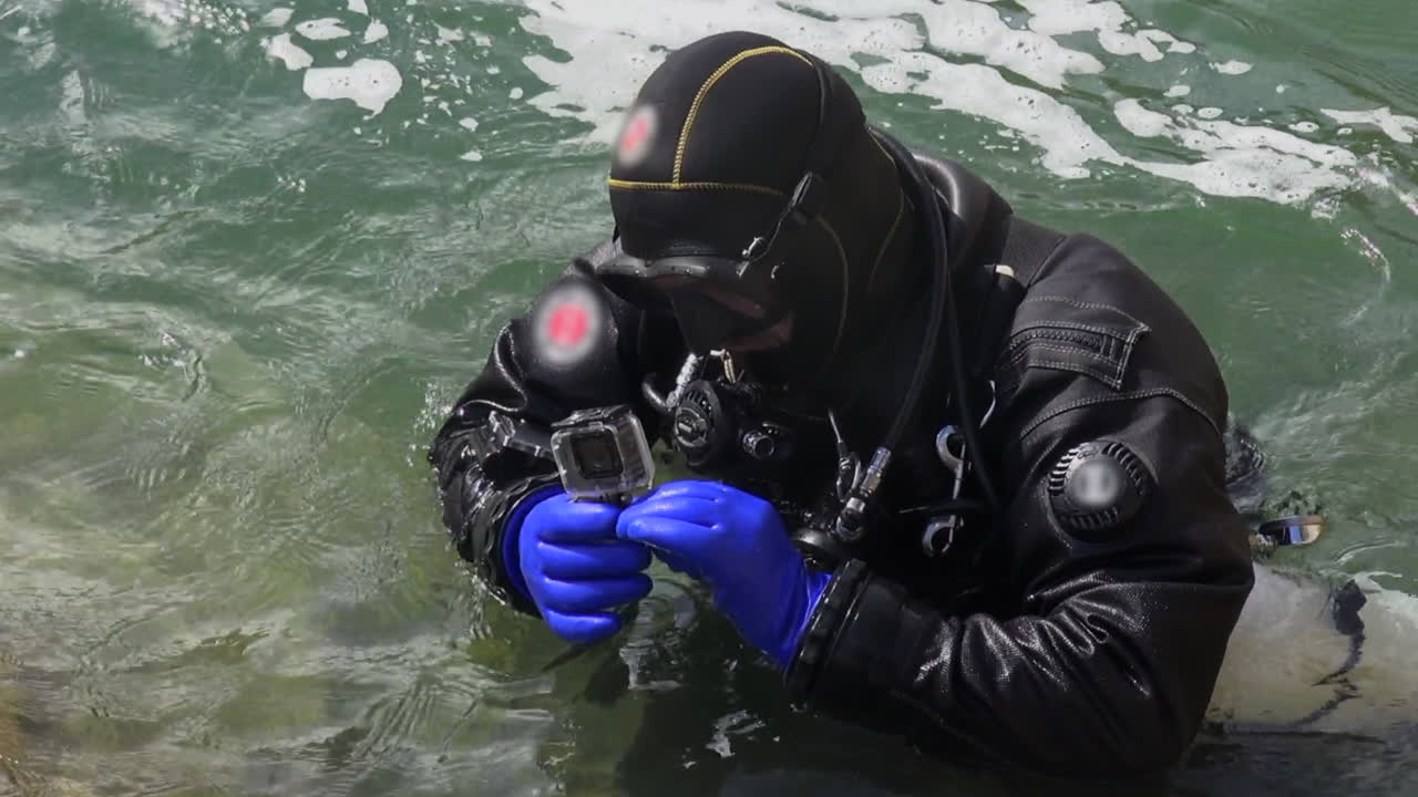 Technical diver in gear inspects underwater camera at chaotic river