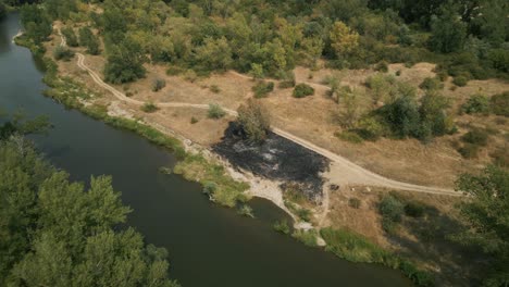 aerial revealing opening shot of burned dry grass by the river on hot summer day, europe