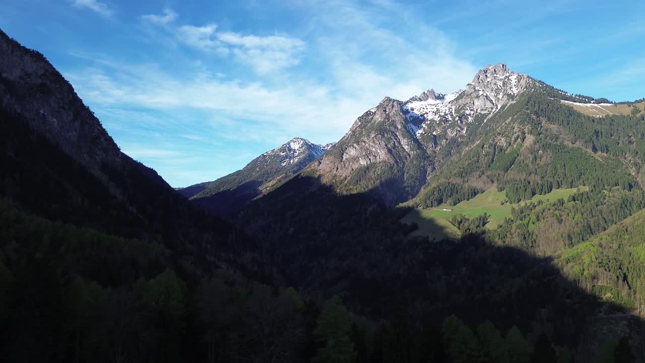 Drohnen-Luftaufnahme über Wald und Berg mit schneebedecktem Gipfel an einem sonnigen Tag mit blauem Himmel in Österreich, Europa