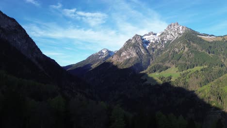 Drone-Aerial-View-over-Forest-and-Mountain-with-Snowy-Summit-on-a-sunny-day-with-blue-sky-in-Austria,-Europe