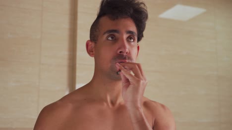 serious young man brushing his teeth in front of a bathroom mirror