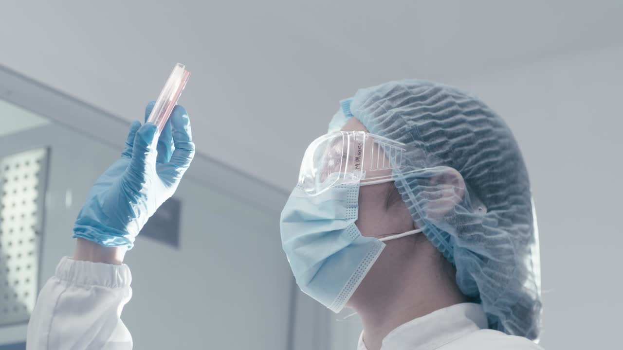 Female scientist wearing a mask and glasses checking an object that has been observed under a microscope in a modern research laboratory