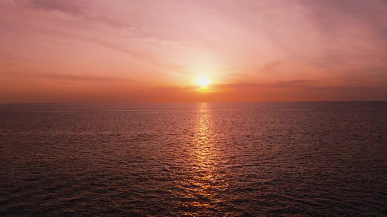 Drone flying over ocean toward glowing sunset in Phuket Thailand
