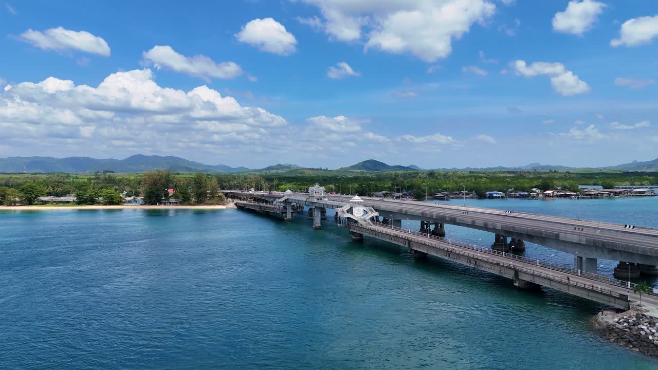 Drone footage captures Sarasin Bridge in Phuket, Thailand, under clear skies, showcasing the bridge's structure and surrounding tropical landscape