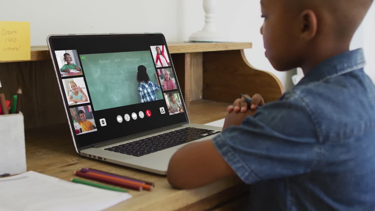African american boy holding a pencil having a video conference on laptop at home