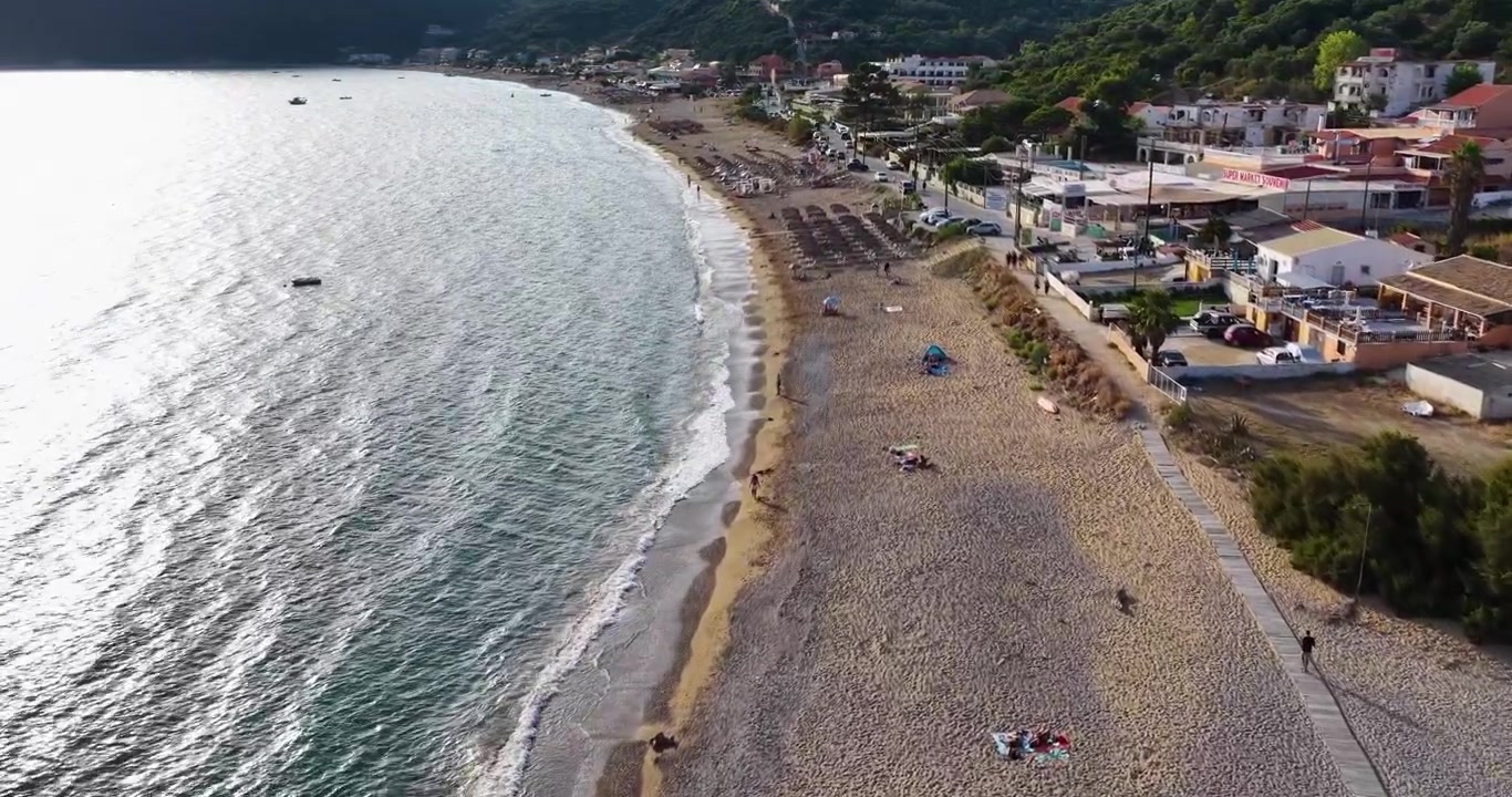 Ripresa aerea con drone della costa della spiaggia di Agios Georgios Pagon a Corfù, Grecia, con la luce del sole che si riflette sulle onde scintillanti del mare e sulla costa sabbiosa