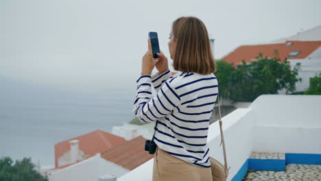 chica tomando fotos con su teléfono inteligente en la ciudad marítima verticalmente. blogger explorando la ciudad