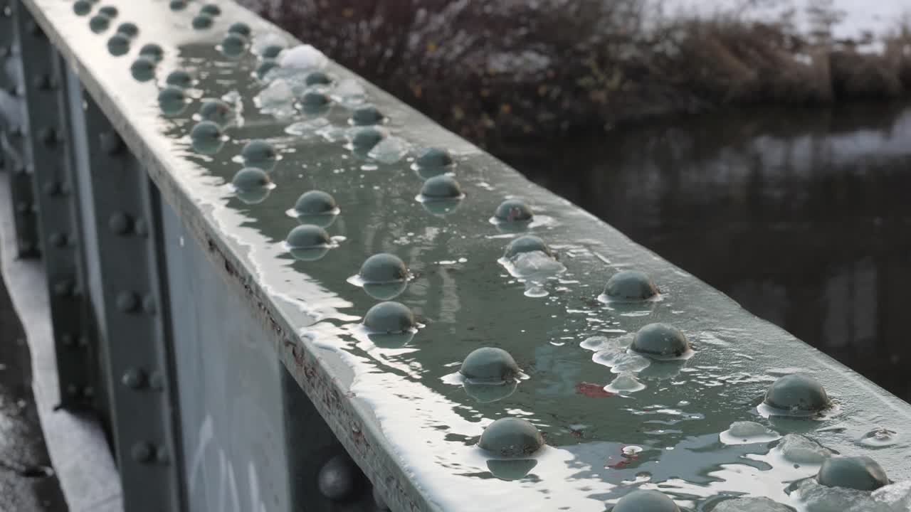 Grey bridge railing during the day with snow and water, close up shot