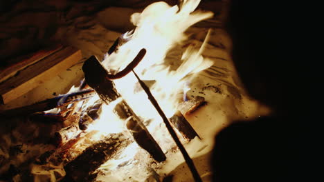 hands holding a stick over the fire with sausage