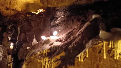 slow panning shot of small candles burning in a cave at night