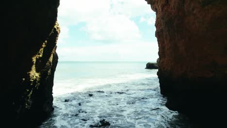 Drone-4k-view-through-picturesque-beach-cave-to-see-the-gentle-waves-and-vast-ocean-at-Praia-Dona-Ana-near-Lagos-in-the-Algarve-region-of-Portugal