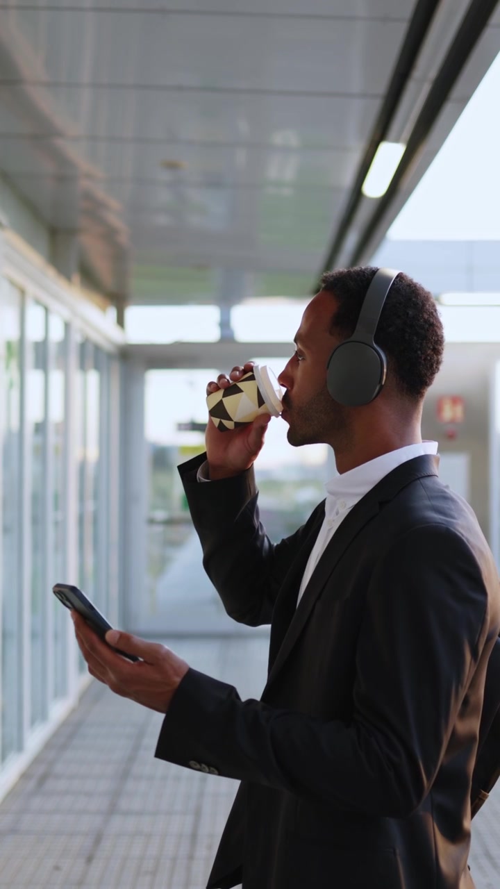 Ung professionel mand bruger smartphone og drikker kaffe i moderne korridor