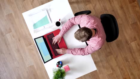 young man in glasses typing on laptop people walking around, topshot, sitting behind desk, busy, circling around view