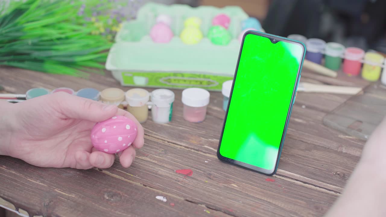 A man prepares for Easter, paints Easter eggs and uses a smartphone with chroma key