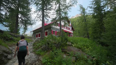 woman trekking in summer season toward red colored mountain refuge of alpe ventina in valmalenco, italy