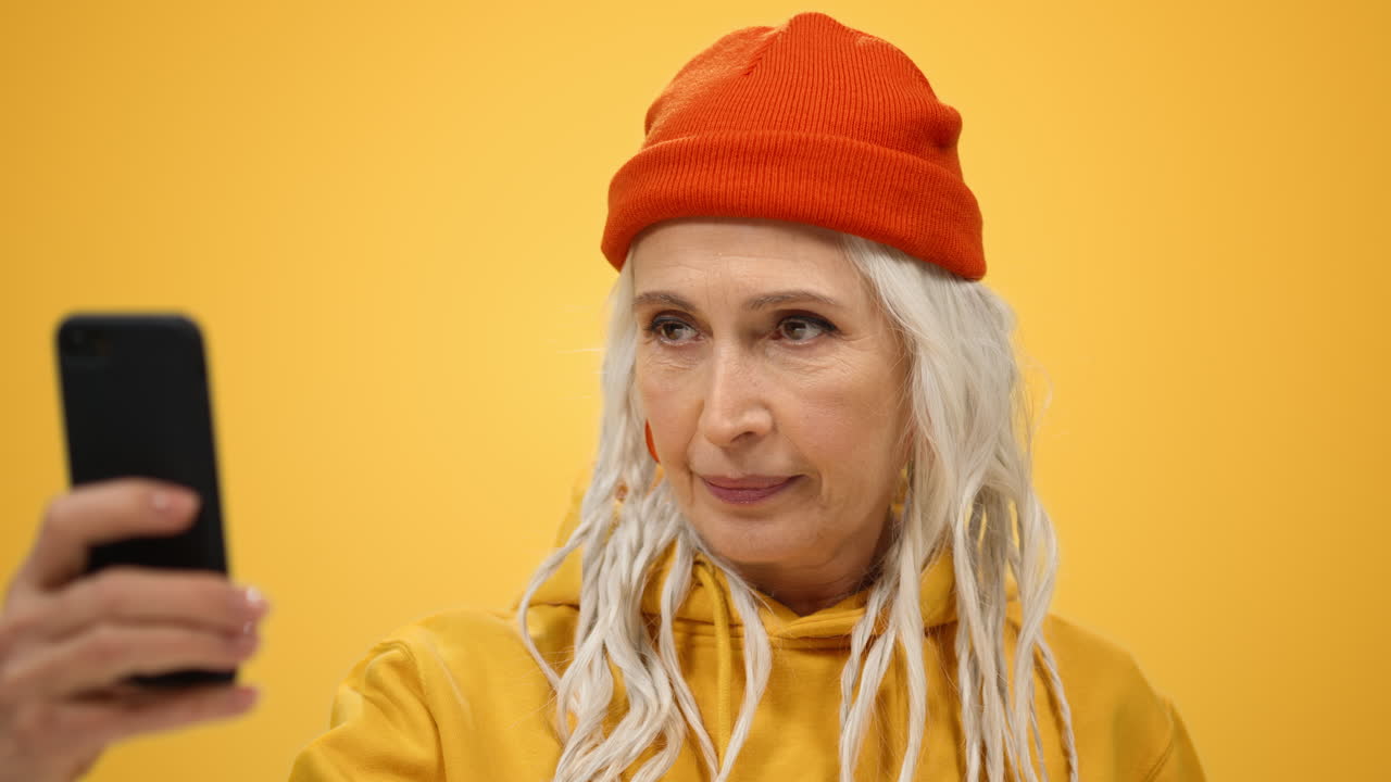 실내에서 셀카를 찍는 행복한 여성. 스튜디오에서 휴대폰 카메라를 흔드는  ⁇ 은 여성.