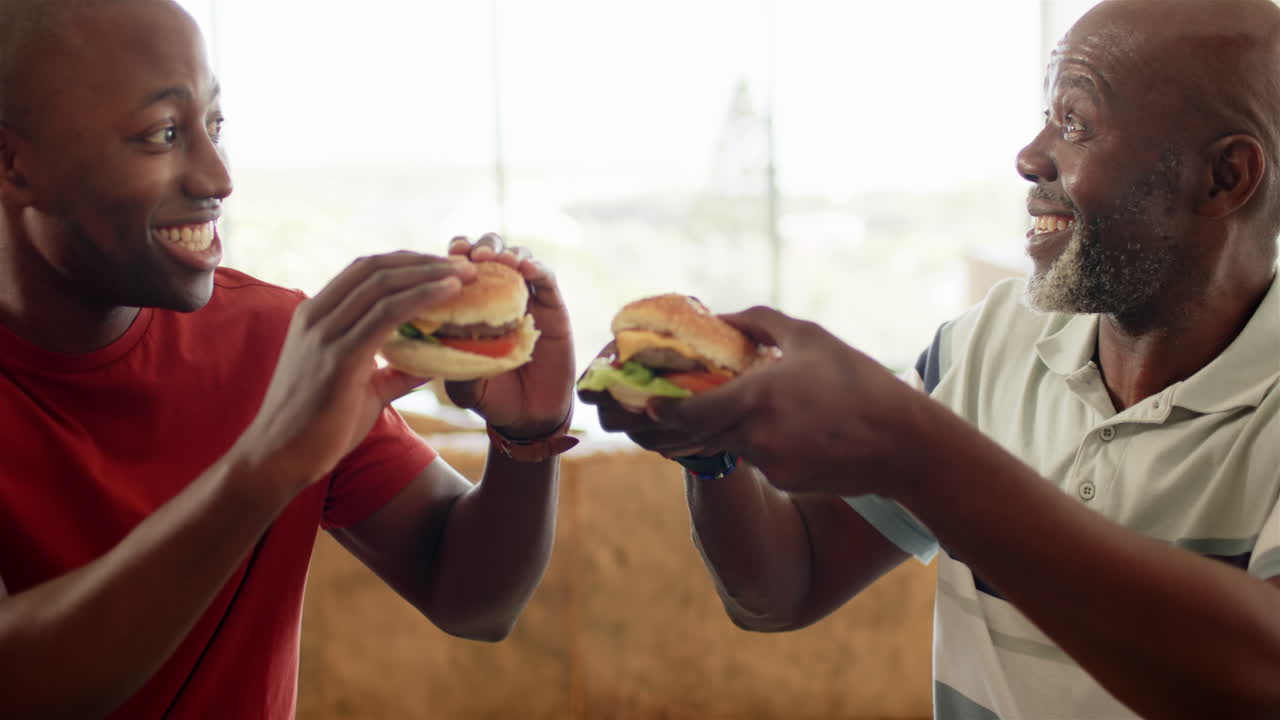 Enjoying burgers together, smiling men sharing joyful moment indoors