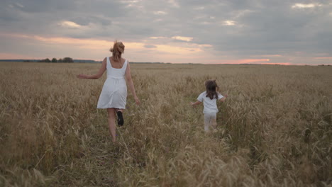 Tochter-Und-Mutter-Träumen-Gemeinsam-Davon,-Bei-Sonnenuntergang-Im-Weizenfeld-Zu-Laufen.-Glückliche-Familienmenschen-Im-Weizenfeldkonzept.-Mutter-Und-Mädchen-Spielen-Aufholjagd.-Baby-Kind-Spaß-Beim-Laufen-Auf-Der-Grünen-Wiese.