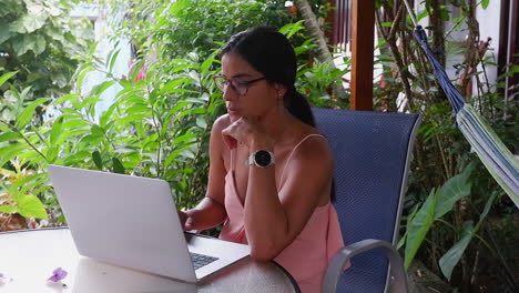 Latina-woman-with-long-dark-hair-works-on-laptop-in-jungle-cabana