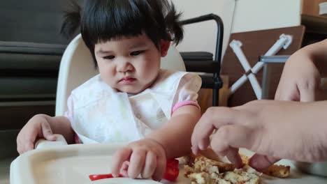 linda niña asiática comiendo su comida casera en una silla de alimentación para bebés