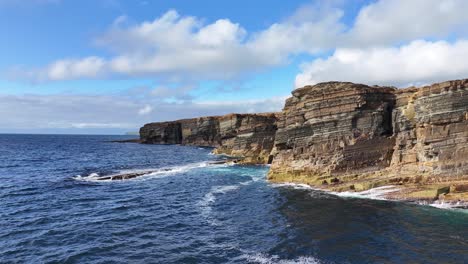 Drone-Shot-of-Scenic-Coastline-of-Scotland-UK,-Sea-Waves-Crashing-Under-Steep-Cliffs-on-Sunny-Day